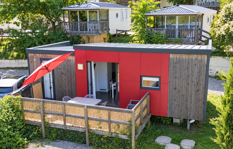 Bungalow rouge et bois avec terrasse et parasol, vu du dessus, au camping